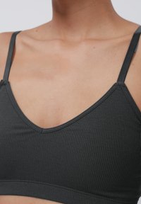 Gray ribbed bralette with a V-neck design and thin adjustable straps. Fabric appears soft, with a smooth texture and a fitted silhouette.