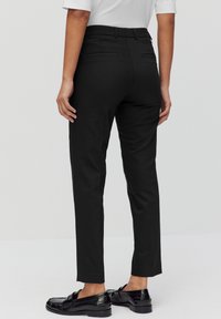 Zwarte op maat gemaakte broek met een slim fit, voorzien van een mid-rise taille en twee achterzakken, gecombineerd met zwarte schoenen, gladde textuur.
