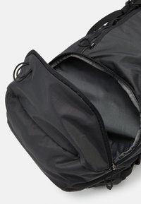 Černý nylonový batoh s hladkou texturou, vybavený zipovým otvorem, nastavovacími popruhy a kompaktním designem pro snadné nošení.
