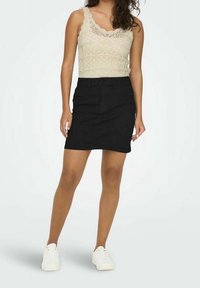 Black denim skirt with a fitted shape, featuring a mid-rise waist and front pockets, paired with a cream, lace-textured tank top and white sneakers.