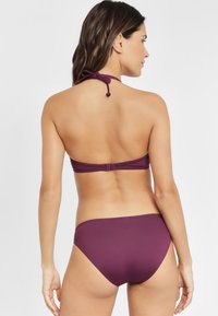 Bikini set van twee delen in een diepe pruimenkleur, met een halternekbandje en bijpassende bikinionderkant. Gladde textuur met minimale hardwaredetails.
