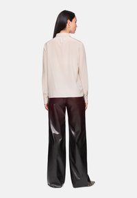 Beige silk blouse with a collar, featuring long sleeves and a curved hem, paired with high-waisted, shiny black leather wide-leg pants.