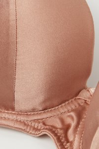 Saténová podprsenka v jemné růžové barvě s hladkou texturou. Má tvarované košíčky, jemné švy a mírně nařasený okraj pro tvarování.