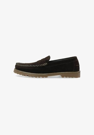 Mocassin en daim brun foncé avec des détails cousus sur le dessus et une semelle en caoutchouc marron clair rainurée, vu de profil sur fond blanc.