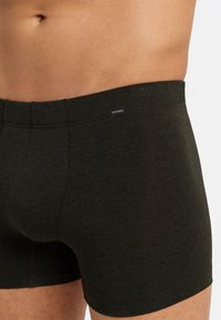 Tmavě zelené boxerky vyrobené z měkké tkaniny. Mají ploché švy a malé logo značky na pase. Přiléhavý design, hladká textura.
