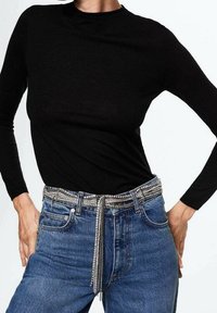 Haut noir à manches longues associé à un jean en denim bleu. La ceinture présente un motif de strass argenté avec un détail de chaîne pendante.