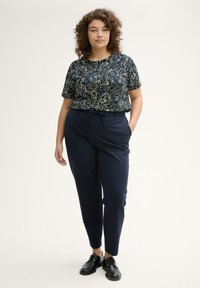 Camicetta nera a maniche corte con motivo a pois multicolore abbinata a pantaloni sartoriali blu navy e scarpe nere stringate.