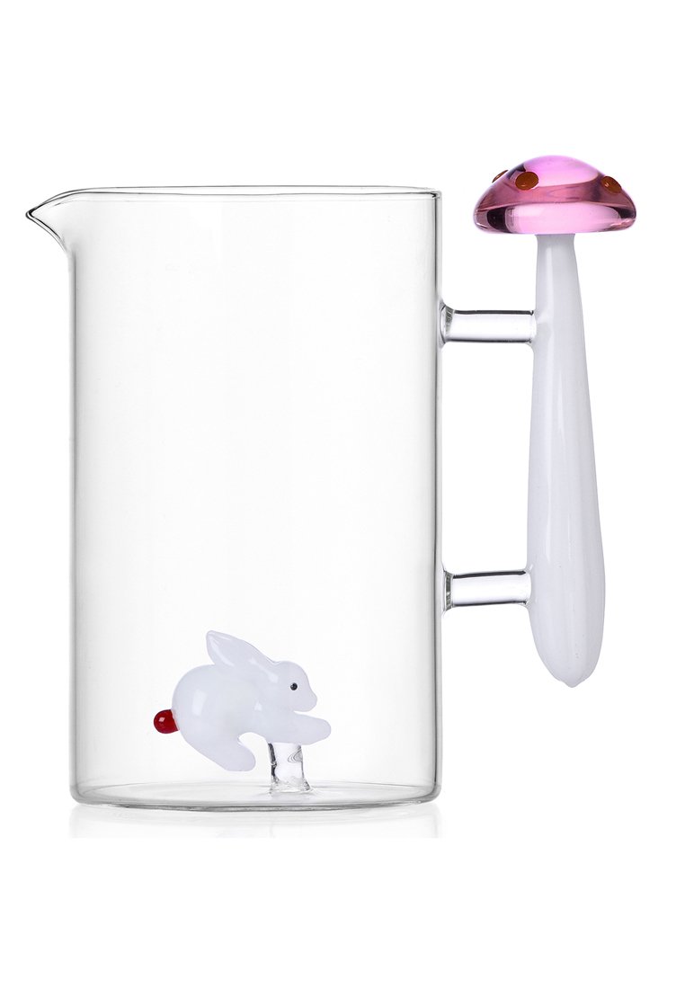 Przezroczysty dzbanek szklany z figurką białego królika na dnie oraz uchwytem w kształcie różowej grzyby.