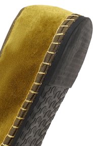 Zbliżenie na żółtą zamszową podeszwę buta z czarnym gumowym bieżnikiem i widocznym przeszyciem wzdłuż krawędzi.