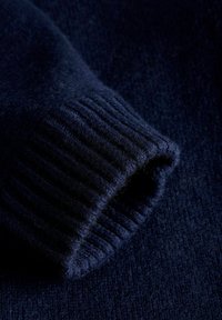 Morski niebieski dzianinowy sweter z mankietem o prążkowanej teksturze, miękkiej tkaninie i bezszwowym przejściu do głównej części, ukazujący równą powierzchnię.
