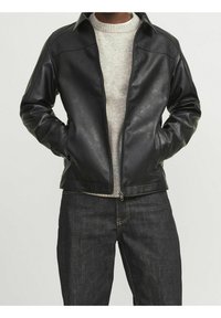 Svart läderjacka med dragkedja fram, skräddarsydd passform och ståkrage, över en ljusgrå crewneck-tröja. Mörka jeans synliga.