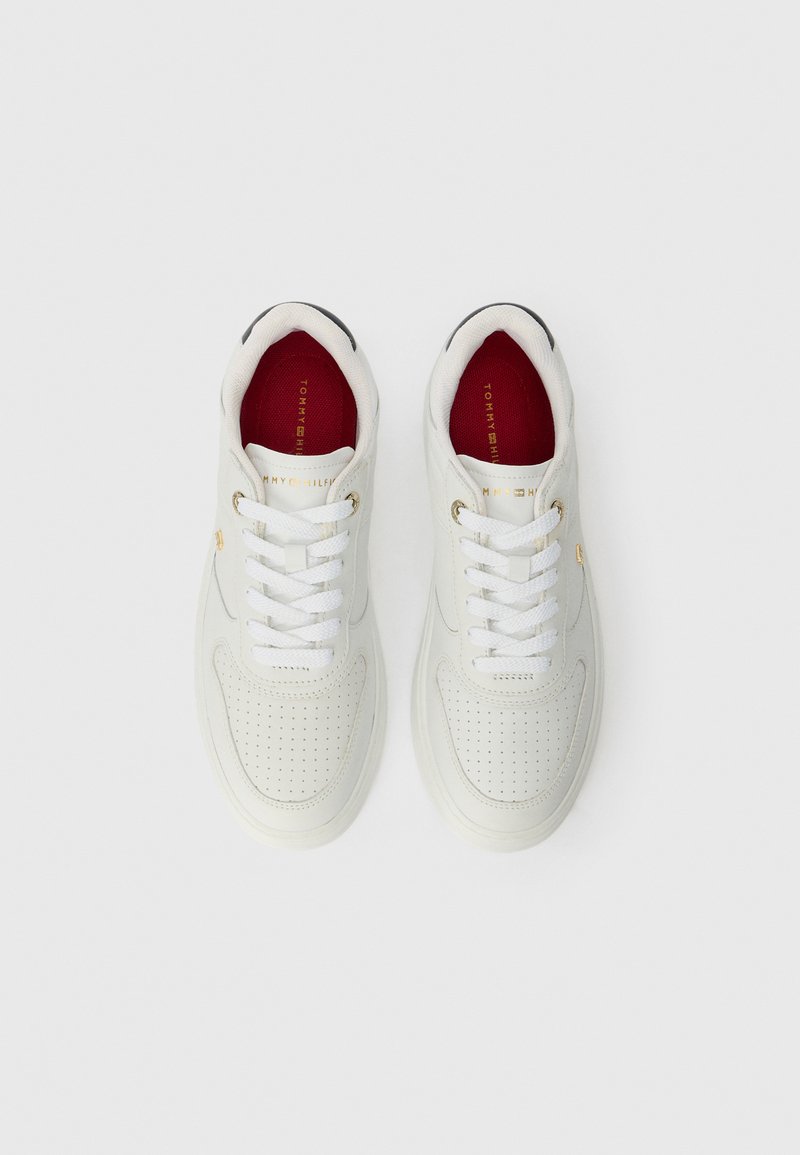 Zapatillas de cuero blancas con diseño perforado, que cuentan con cordones blancos y un interior rojo. Detalles en dorado adornan los lados. Suela plana.