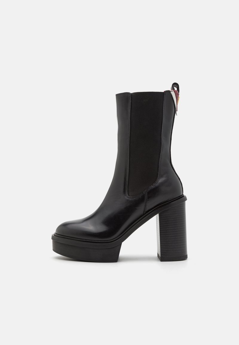 Zwarte enkelboot met een glanzend leren bovenkant, elastische zijpanelen en een chunky, gestructureerde plateau hak. Heeft een lus aan de achterkant.