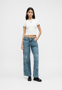 Λευκό κοντό t-shirt με μικρό λογότυπο. Ανοιχτό μπλε τζιν παντελόνι με φαρδιά μπατζάκια και διακριτικό γραφικό σχέδιο. Μαύρα επίπεδα παπούτσια με υφασμένο σχέδιο.