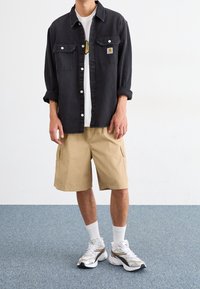 Black denim button-up shirt with two chest pockets, khaki cargo shorts, white t-shirt, and chunky white/gold athletic shoes.
