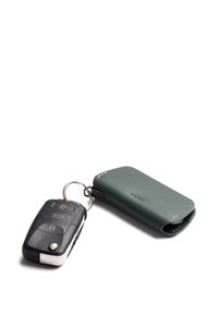 Porte-clés avec boutons en plastique noir et accents argentés, accompagné d'un étui en cuir vert foncé avec des détails cousus et une forme arrondie.