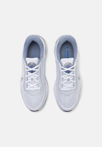 White athletic shoes with a textured upper, padded tongue in light blue, reflective accents, and laces. Feature a circular logo and design detailing.