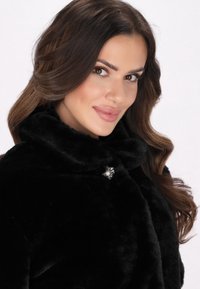 Palton negru din blană sintetică cu guler înalt, având un accent floral argintiu. Textură netedă, aspect moale și croială îngrijită.