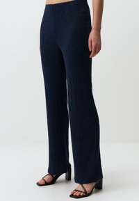 Pantaloni a gamba larga blu navy, a righe, realizzati in un tessuto testurizzato. Presentano una vita alta e una silhouette rilassata, abbinati a sandali neri con tacco.