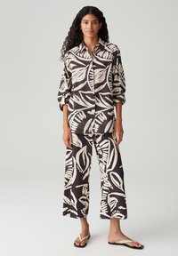 Camicia nera e panna con motivo a foglie e pantaloni a gamba larga coordinati, entrambi realizzati in tessuto leggero con una consistenza liscia. Includono ciabatte.