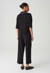 Schwarzes Kurzarm-Oberteil mit weißem Piping, kombiniert mit weiten schwarzen Hosen. Die Schuhe haben ein schwarzes Netzdesign mit einem Akzentdetail.