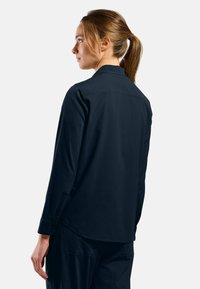 Navy long-sleeve shirt with a collar, buttoned cuffs, and a curved hem. Fabric appears smooth, and back features a yoke detail.