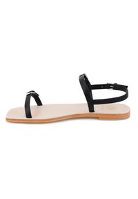 Zwarte leren platte sandalen met dunne bandjes, een minimalistisch ontwerp en een lichtbeige zool met subtiele textuur en een houten accent.