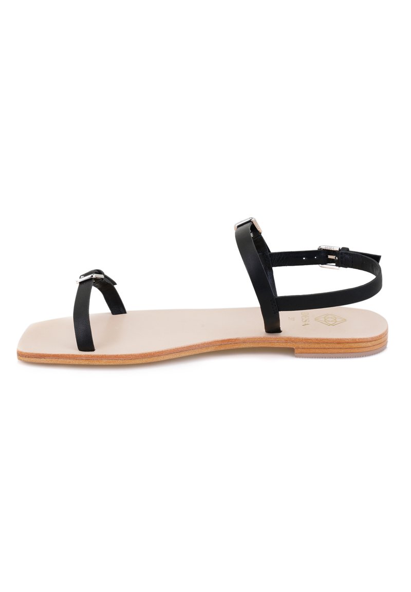 Zwarte leren platte sandalen met dunne bandjes, een minimalistisch ontwerp en een lichtbeige zool met subtiele textuur en een houten accent.