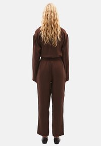 Hnědý, volně střižený dvoudílný outfit s dlouhými rukávy a širokými kalhotami, vyrobený z texturované látky, s elastickým pasem.