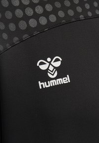 Svart idrottstopp med en strukturerad yta som har stora grå prickar. Vit "hummel"-logotyp och grafisk accent på framsidan.