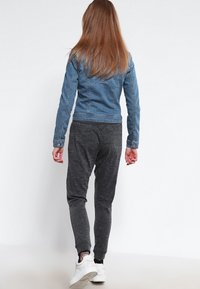 Chaqueta de denim con un diseño ajustado, de color azul; combinada con pantalones jogger grises. El modelo se ve desde atrás, mostrando calzado atlético casual.