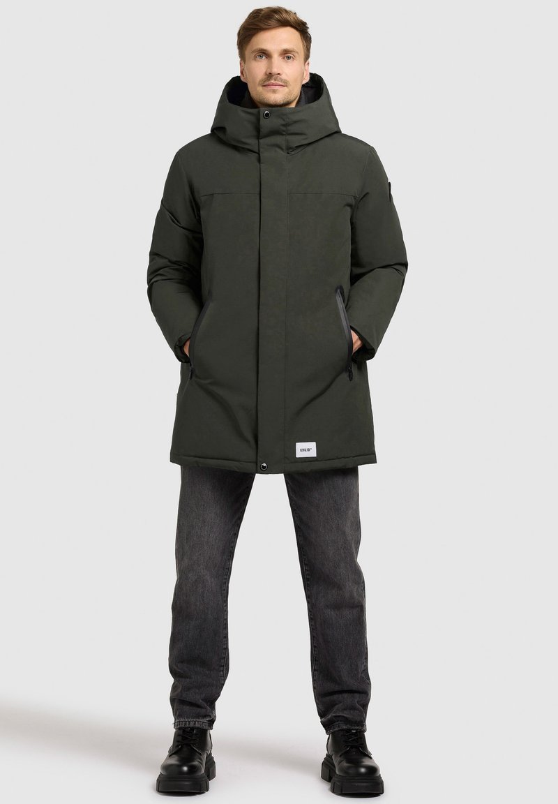 Zelena parka jakna s visokim ovratnikom i kapuljačom, sa crnim detaljima, dva prednja džepa i logotipom na rubu.
