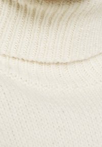 Crème-kleurige gebreide trui met een geribde col en een zachte textuur. De stof heeft een fijne, rekbare weving.