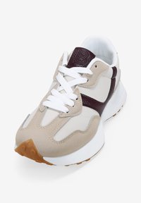 Zapatilla beige y blanca con un acento texturizado en color marrón, que presenta una puntera redonda, cordones en la parte delantera y suela de goma con un diseño de relieve.