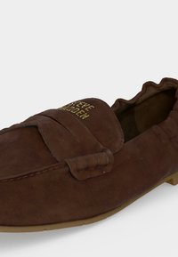 Καφέ καστόρινο loafer χωρίς κορδόνια με ελαστική πίσω ζώνη και χρυσό λογότυπο "Steve Madden" στο πάνω μπροστινό λουράκι, ορατή καφέ σόλα.