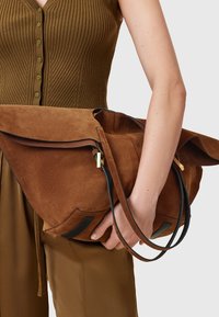 Grande borsa in suede marrone con una forma strutturata, caratterizzata da dettagli in pelle nera, doppio manico e chiusura a piega.