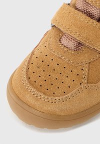 Pruunist suede'ist kingad, millel on velcro rihm, perforatsioonid varbaosas ja kummist tald. Nähtavad tekstureeritud kangakatted.