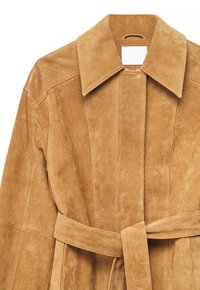 Kabát z broskytovej semišovej kože s širokým golierom, prešívanými vertikálnymi panelmi a zladeným opaskom previazaným v páse, zobrazený z prednej hornej časti.