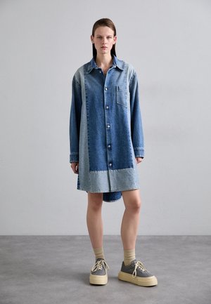 Denim mekko, jossa on sekoitus vaaleaa ja tummaa pesua, napitus edessä, kauluspaita-kaulus ja rintatasku. Pehmeä rakenne, pitkät hihat ja epäsymmetrinen helma.