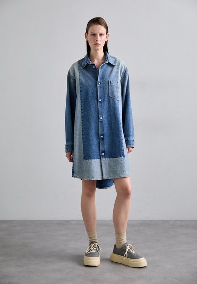 Denim haljina košulja s kombinacijom svijetlog i tamnog pranja, prednjim kopčanjem, ovratnikom i džepom na prsima. Mekana tekstura, duge rukave i asimetrični rub.