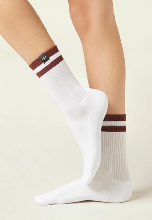 Pair of white ankle socks with maroon stripes worn on feet against a light background, one foot slightly raised.