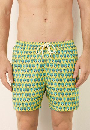 Badehose mit einem leuchtend gelben Hintergrund und einem wiederholten Kaktusmuster in Blau und Grün. Mit einem verstellbaren Bund mit weißen Akzenten.