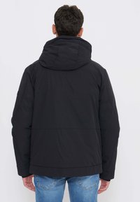 Sort puffervest med hætte, der har en glat, mat overflade, en ren silhuet og kontrasterende syningsdetaljer.