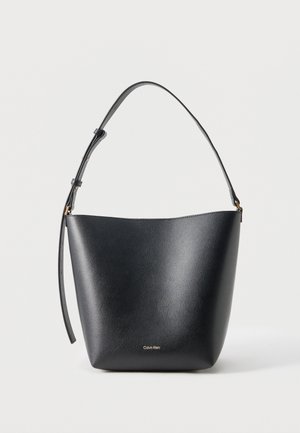 Czarna skórzana torba typu bucket z regulowanym paskiem na ramię i małym złotym logo Calvin Klein na przodzie.