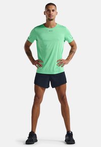 Camiseta deportiva de color verde menta con cuello redondo y mangas cortas, combinada con shorts negros y zapatillas negras. Presenta un diseño texturizado.