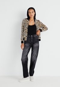 Bomber bunda s leopardím vzorom a čiernymi detailami, spárovaná s čiernymi rifľami s vysokým pásom a bielymi teniskami. Hladká tkanina a voľný strih.