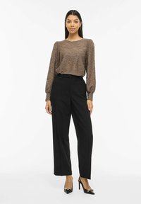 Haut marron texturé à manches longues avec un motif ondulé, associé à un pantalon large noir taille haute et des chaussures à talons noires.