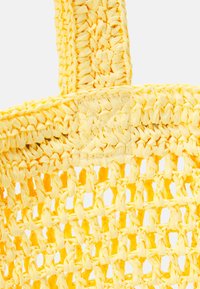 Sac cabas tissé jaune en matériau semblable à de la paille. Il dispose de poignées épaisses et texturées et d'un motif de tissage ouvert, soulignant un design léger.