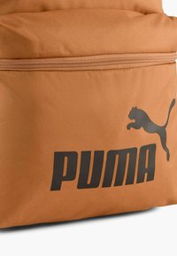 Mochila PUMA de tela naranja con un gran logo negro y la silueta de un gato saltando, que cuenta con un compartimento con cremallera para almacenamiento.