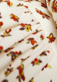 Tissu crème avec couture froncée et motif floral en rouge, jaune et violet foncé dispersé sur la surface.